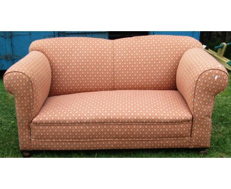 An Edwardian two seat sofa with rolled arms and single drop end, upholstered in repeating floral lattice pattern fabric and r