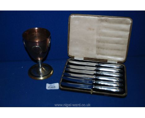 A cased set of silver handled butter knives and a brass and copper goblet inlaid with old coins.
