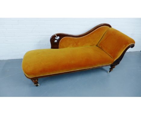 A Victorian mahogany framed chaise longue upholstered in amber coloured fabric, raised on turned supports terminating in cera