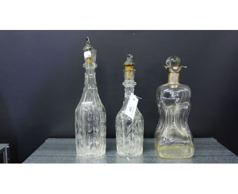 Two facet cut bottle neck glass decanters, each with a pewter vine leaf and fruit embossed stopper together with a gurgle dec