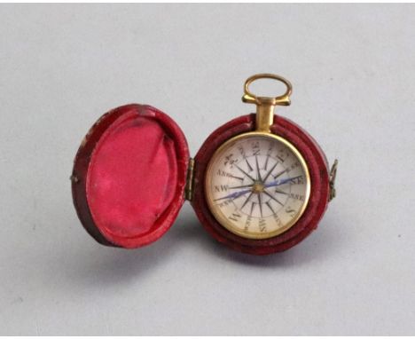 A George III gilt metal cased pocket compass, 2.5cm diameter, with hinged suspension ring, in red morocco leather covered car