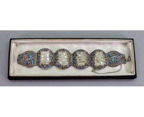 A carved jade panel link bracelet, the four jade panels carved and pierced in varied designs, each within an enamel and filig