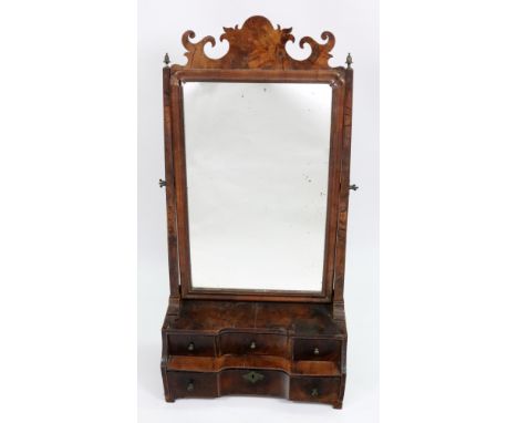 An early 18th century walnut swing toilet mirror, the moulded frame with a shaped fret carved surmount, the stepped concave f