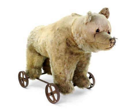 An early 20th century blonde plush bear, on cast iron wheels, possibly Steiff, 70cm wide x 46cm high.