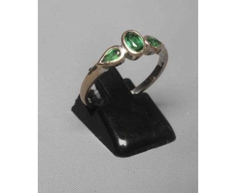 A THREE STONE TOURMALINE RING, the central oval facet cut stone flanked by two tear cut stones all in open collet mounts to a
