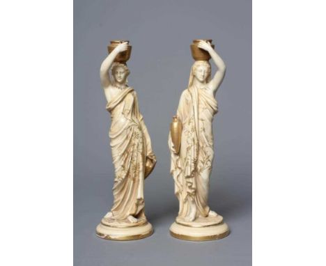 A PAIR OF ROYAL WORCESTER PORCELAIN FIGURES OF WATER CARRIERS, 1912, each female wearing a gilded draped robe and carrying a 