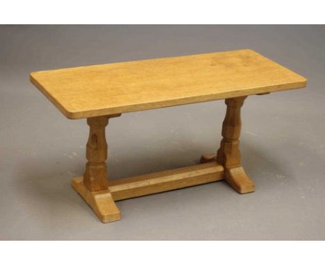 A ROBERT THOMPSON ADZED OAK COFFEE TABLE, the rounded oblong plank top raised on two baluster turned faceted legs, the trestl