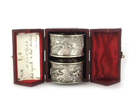 A cased pair of white metal napkin rings depicting hunting scenes. Approx weight 78 grams CONDITION REPORT: Marks to case. Li