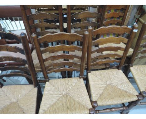 A set of three oak vernacular style kitchen chairs having ladder backs and rush seats and a similar set of four chairs