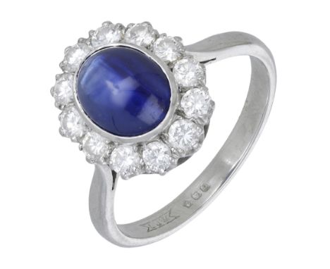 A sapphire and diamond cluster ring, 1985, the sapphire cabochon set within a surround of brilliant-cut diamonds, London hall