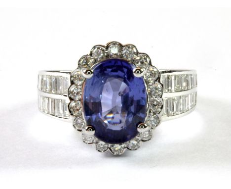 An 18ct white gold ring set with an oval cut sapphire and diamonds, (approx. S. 3.06ct and D. 1.03ct), (K).