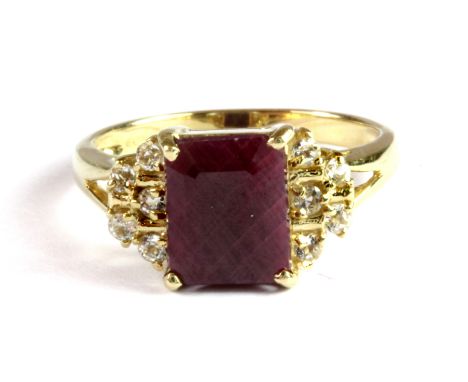 A 9ct yellow gold ring set with an emerald cut ruby and diamond set shoulders, (N.5).