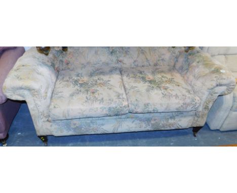 A two seater Chesterfield sofa, upholstered in a floral fabric, raised on legs and castors.