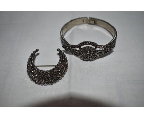 A cut steel tension bangle having pierced lozenge shaped panel and concealed clasp and a similar cut steel crescent brooch