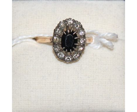 An 18ct gold sapphire and diamond cluster ring, claw set with a mixed cut stone bordered by brilliants
