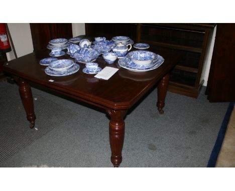 An Edwardian walnut extending dining table of oblong form with canted corners and turned and fluted legs with brass and ceram