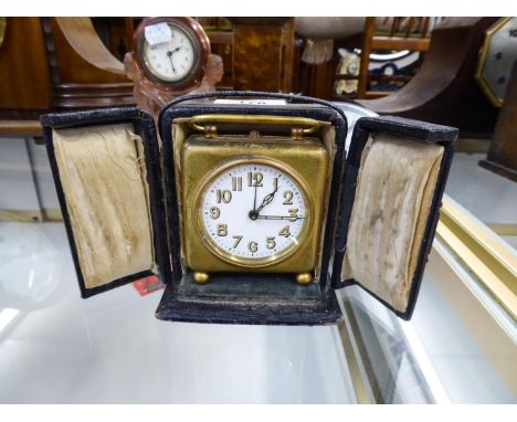GILT METAL CASED TRAVELLING BEDSIDE CLOCK with carrying handle, contained in an outer leather travelling case, with strap han