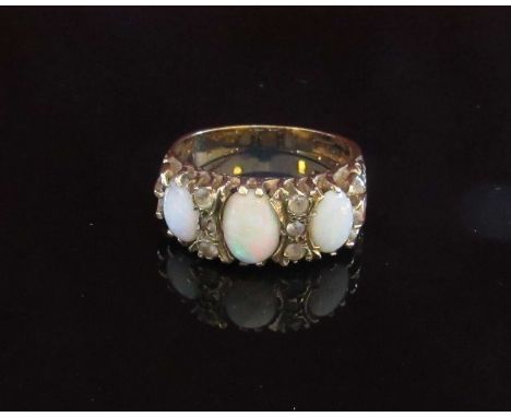 A 9ct gold ring set with three oval opals with scroll engraved shoulders. Size R, 4.6g