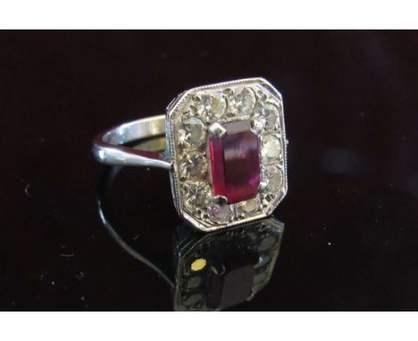 A Platinum ruby and diamond ring, the central emerald cut ruby 8mm x 5mm, framed by 10 brilliant cut diamonds. Size N, 5.6g