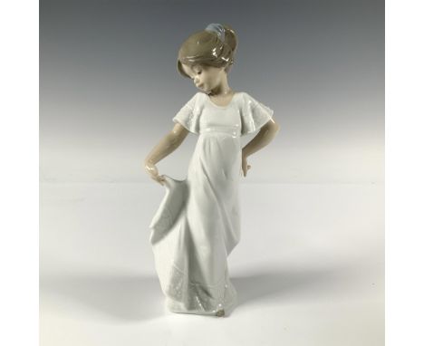 A figurine of a young girl, dressed in white, as she playfully lifts the end of her dress. Nao by Lladro backstamp. Artist: A