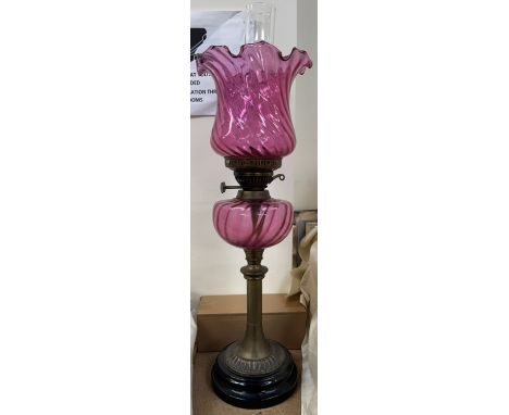 A Cranberry glass oil lamp and shade on a brass column and spreading base 