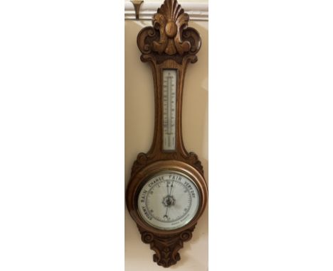 A 19th century oak aneroid barometer with a carved top, mercury thermometer and a porcelain dial 