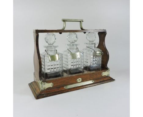 An early 20th century brass mounted oak tantalus, containing three cut glass decanters and stoppers, each with a silver plate