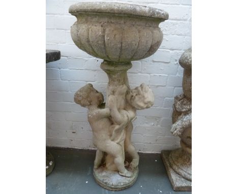 A composite stone planter in the form of a classical urn raised up by two cherubs 90cmH