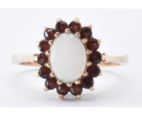 A hallmarked 9ct gold opal and garnet cluster ring.&nbsp; The ring having a central oval opal cabochon surrounded by round cu