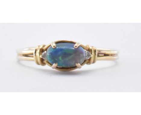 A 14ct gold and black opal and diamond ring. The ring being set with on oval cabochon flanked by two round cut diamonds. Band