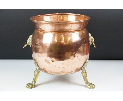 Copper Planter / Jardiniere of cauldron form with two brass lion mask drop ring handles and raised on three brass lion paw fe