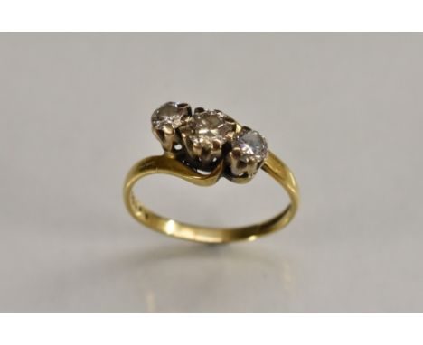 A twisting crested diamond trilogy ring, central round brilliant cut diamond flanked by a smaller conforming stone either sid