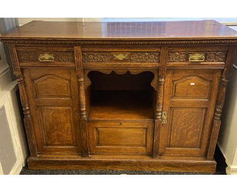 Oak dresser base, long central carved drawer above an open shelf and base cupboard, flanked by two matching short drawers and