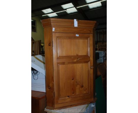 A stained pine corner wall hanging cabinet with two shelves and a panel door.