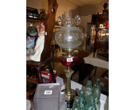 A brass Corinthian column oil lamp with cranberry glass font and later shade