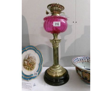 A brass oil lamp with Corinthian column and cranberry glass font (no shade or chimney)
