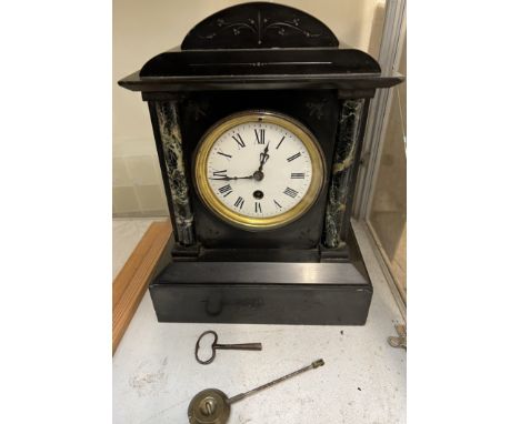 A black slate mantle clock with a bowed top and variegated columns on a plinth