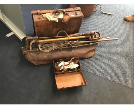 A vintage leather suitcase and sporting accessories: roller skates, shooting stick, Lacrosse sticks, cricket etc