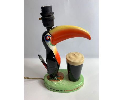 A Carltonware Guinness ceramic advertising table lamp in the form of a toucan standing on a grassy base with a glass of Guinn