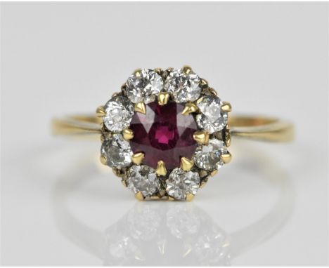 A yellow metal ruby and diamond cluster ring, with a central round cut ruby in an eight claw setting surrounded with a halo o