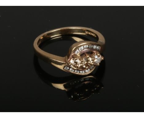 A 9ct gold and diamond crossover ring. Set with three champagne diamonds under channel set borders. 3.2 grams gross, size N. 