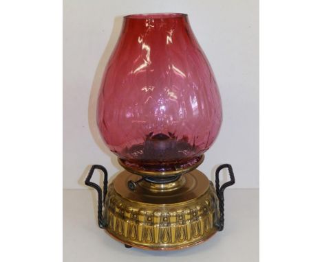 A large brass church oil lamp/heater with cranberry glass shade and two iron handles to the base, 16.5" overall height.