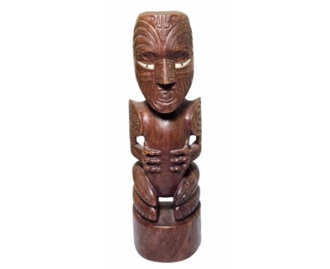 A Maori Tekoteko statue - New Zealand.The wood carved as a crouched male figure atop a curved base, with a large head and thr