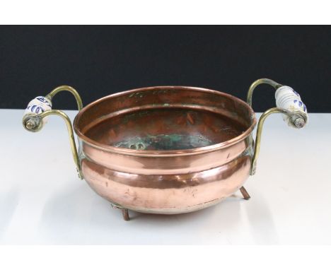 Copper circular planter with rolled rim and twin brass and ceramic handles, raised on three feet, 29cm wide