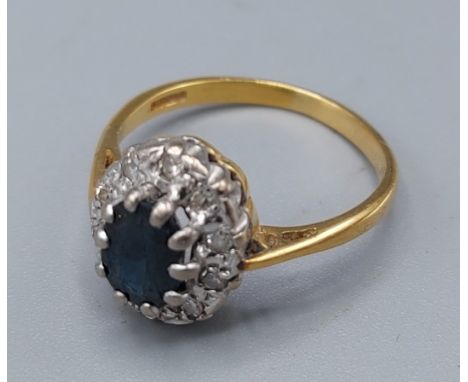 An 18ct gold sapphire and diamond cluster ring with a central oval sapphire surrounded by diamonds, 3.3gms, ring size K 
