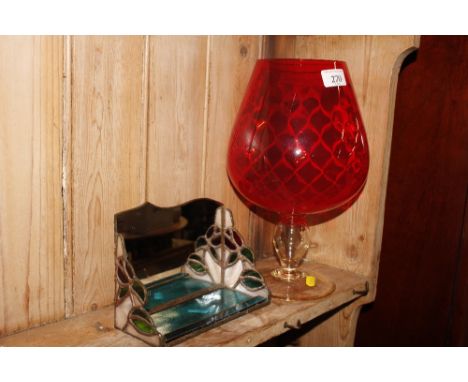 A large red glass goblet and small mirrored shelf 