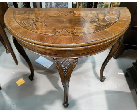 An early 20th century mahogany card table, the demi-lune fold-over top with wide crossbanding and scrolled inlaid decoration,