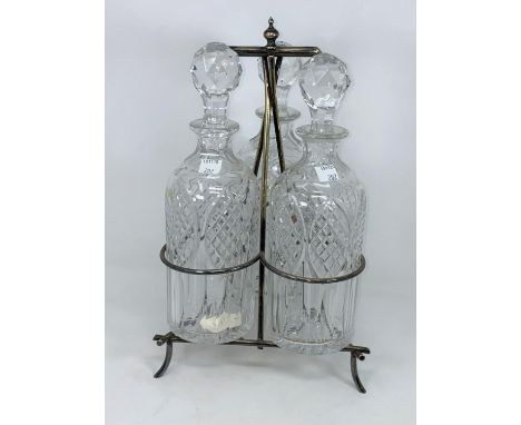 An Arts &amp; Crafts silver plated triple decanter stand with 3 cut bottles 