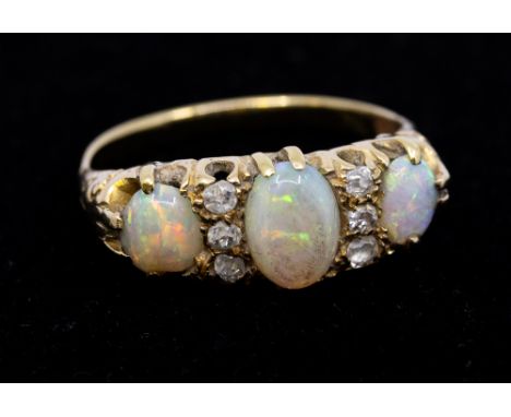 A three-stone opal and six diamond yellow metal ring, comprising three graduated opals, interspersed with old cut diamonds, w