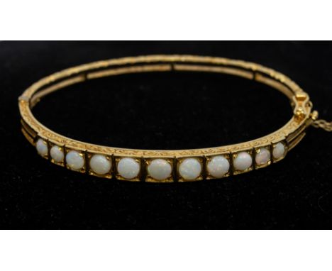 An opal and 9ct gold hinged bangle, comprising a graduated row of round cabochon opals, scrolled decoration to sides, interna
